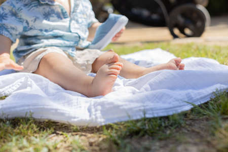 A little child in a park in Spain, during a sunny day, seated berefoot in the grass. He is playing with his skyblue shoes. He is caucasian. He is about ten month old.の写真素材