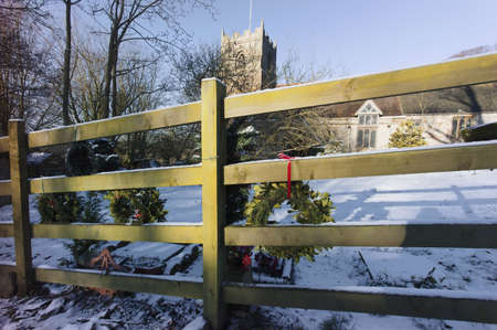 a churchyard and church with wreaths hanging on fence with a snow covered cemetery behind and a clear blue skyの写真素材