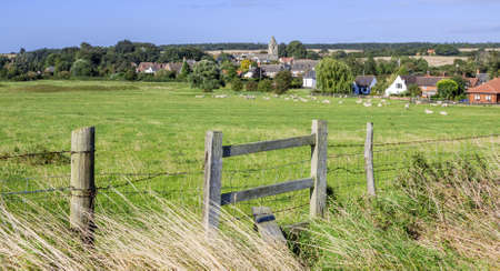 a stile and gate with a village in the distance in the english countrysideの写真素材