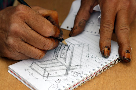 Close-up of an old man's hand drawing a house on a sketchbookの写真素材