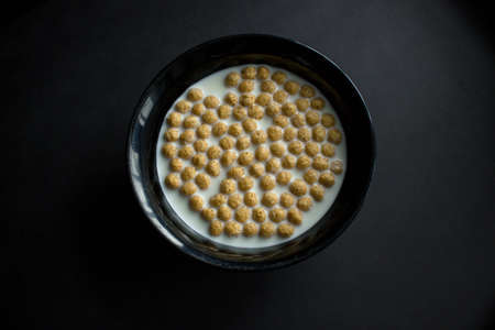 Bowl of cornflakes on dark background.