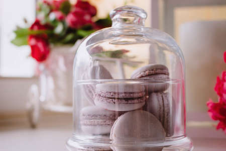 Green, pink and yellow french macarons under the glass on the wooden boards, soft focus background