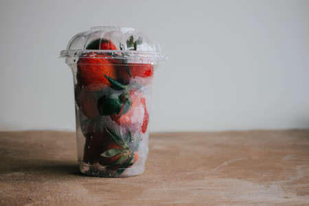 Strawberry In a plastic transparent Cup on a brown wooden table. Healthy breakfast.の写真素材