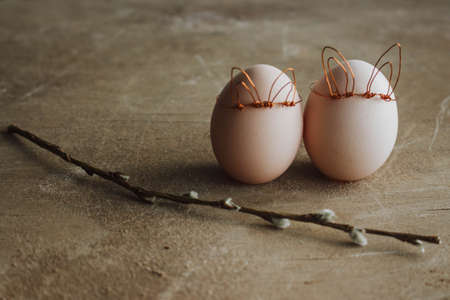 Bunch of white eggs with willow branch and bunny ears on wooden background