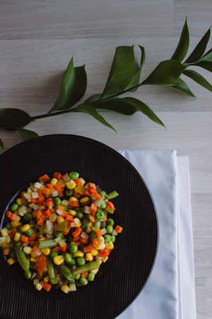 Frozen fried vegetables on black plate. Vegan breakfast. Vegetables food mix on white wooden background.の写真素材