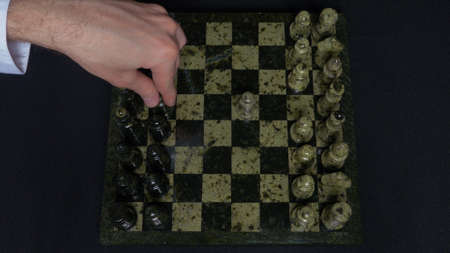 Checkmate. Start Of A Chess Game,the Figures Are Lined Up And A Person Makes The First Move. Hand moving a knight chess piece on chessboard. Mans hands play chess, checkmate in chessの写真素材