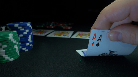 Person showing his deck at the poker game. Card player checks his hand, two aces in, chips in...