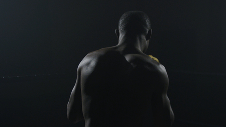Rear view of muscular man boxing on black background. Afro american young male boxer practicing shadow boxingの写真素材