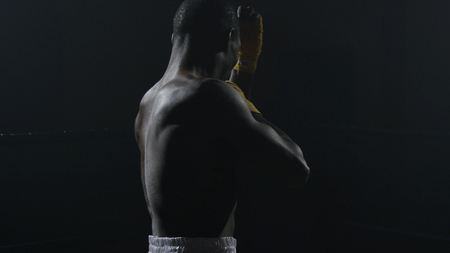 Rear view of muscular man boxing on black background. Afro american young male boxer practicing shadow boxing. Boxer in yellow Boxing glovesの写真素材