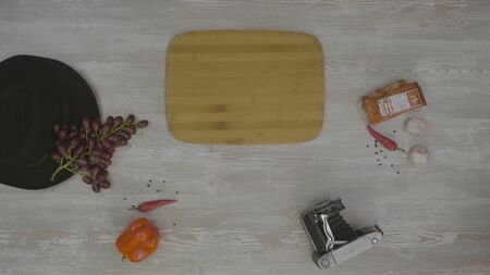 Square wooden board on table. On the table are: hat, peppers, tray, camera and hamの写真素材
