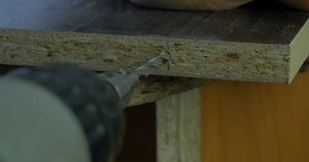 Man holds a drill in his hands and makes a hole in a wooden board. Wood shavings flying around. Close up.の写真素材