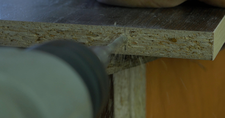 Man holds a drill in his hands and makes a hole in a wooden board. Wood shavings flying around. Close up.の写真素材