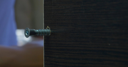 Man using an electric hand drill to drive a screw into a board. Dust motes shine in the air around. Tightening the screw.の写真素材