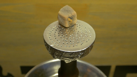 Mans hand puts burning coals on clay bowl with tobacco for hookah, Hookahs head. Hookah topic: Bartender holding a forceps with coal for hookah and puts them into a clay bowlの写真素材