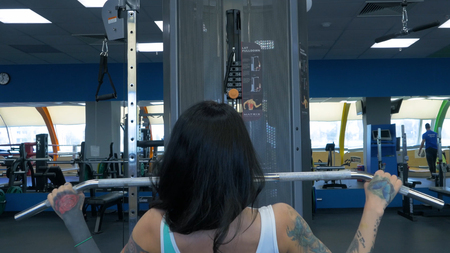Attractive young woman is working out on a fitness station in gym, pumping iron. Outgoing woman...