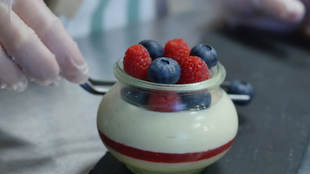 Homemade yogurt with blueberries in a glass jar. Hand putting Strawberry in Yogurt, close up.の写真素材