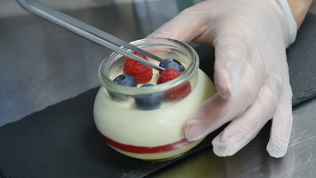 Homemade yogurt with blueberries in a glass jar. Hand putting Strawberry in Yogurt, close up.の写真素材