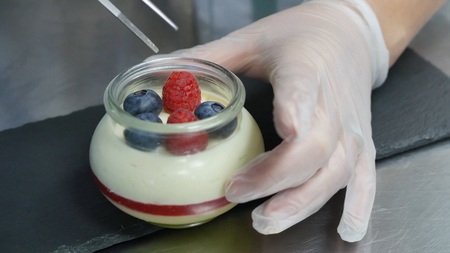 Homemade yogurt with blueberries in a glass jar. Hand putting Strawberry in Yogurt, close up.の写真素材