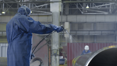 Male holding spray gun and painted steel. Man paints pipe atomizerの写真素材