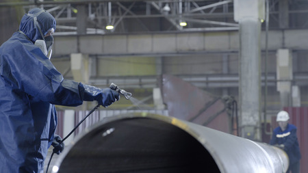 Male holding spray gun and painted steel. Man paints pipe atomizerの写真素材