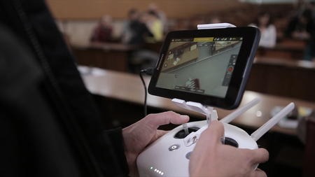Close-up of man's hands with a remote control flying a small quadcopter toy indoors.