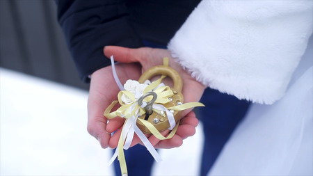 Wedding symbol, lock in hands of bride and groom. Newlyweds fix the lock on the bridge as a symbol of love. Padlock in the hands of the bride and groom. Lock in heart shape on the railing of bridge - a symbol of happy and long married life of bride and grの写真素材