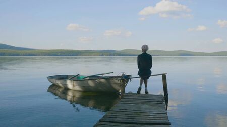 Back view of a woman sitting on a tiny wooden pier by the pond. Young beautiful girl sitting on jetty river on background. Back view.の写真素材