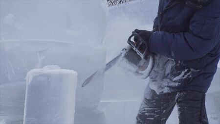 View of sculptor carving ice. Movement. Cut ice with a chainsaw. Cut and make snow sculpture. Chopping iced water with an axe. Ice Sculpture Carving. V-LOGの写真素材