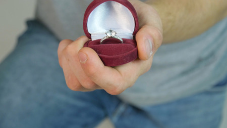 Handsome young man holding box with wedding ring on white background.