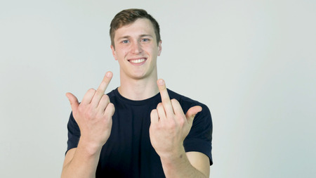 Young Man Showing Middle Finger Isolated on White. Young angry man with black t-shirt looking at camera and showing two middle fingerの写真素材
