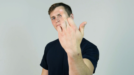 Young Man Showing Middle Finger Isolated on White. Young angry man with black t-shirt looking at camera and showing middle fingerの写真素材