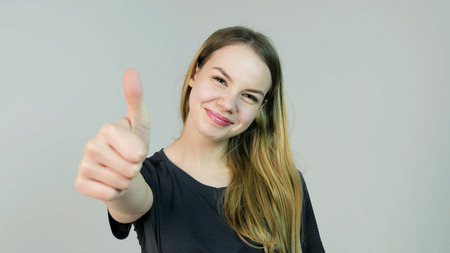 Happy smiling beautiful young woman showing thumbs up gesture on white backgroundの写真素材