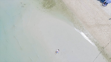 Above angle of happy wedding couple is lying on a tropical sandy beach near the ocean. Aerial view on Attractive Couple Relaxing on Sandy Beach, Tropical Vacation. Young pair lies on to the beach HDの写真素材