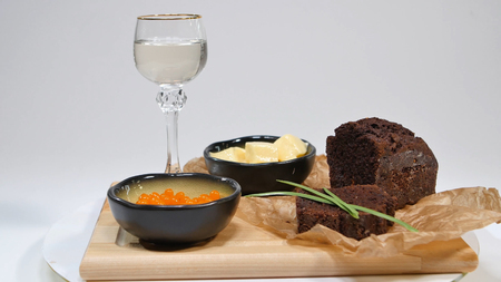 Fresh red caviar with basil and butter on bread in studio. Bred with red caviar with wine glasses on background. Cold Russian vodka with ice and small snacks with butter and red caviarの写真素材