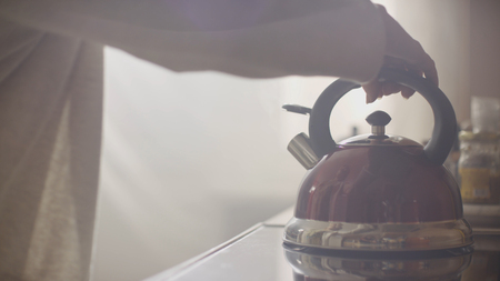 Girl put blue kettle on a kitchen gas stove. Stovetop whistling kettle in handの写真素材