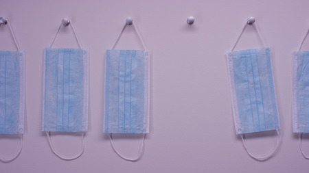 Hand takes protective mask from wall. Surgical Ear-Loop Masks on white wall. A mask for protection...