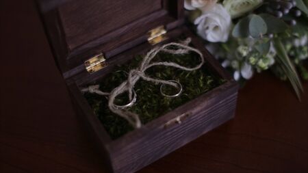 Wedding rings in a wooden box filled with moss on the table. Wooden box with wedding rings lies near the bridal bouquet of the bride from natural flowersの写真素材