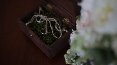 Wedding rings in a wooden box filled with moss on the table. Wooden box with wedding rings lies near...