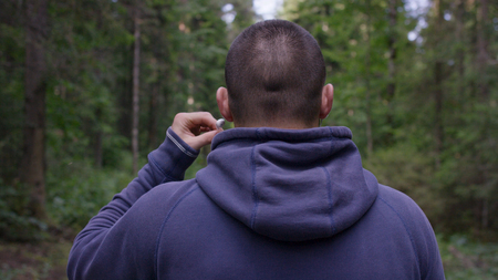 Back view of man standing with headphones and listening music in forest.