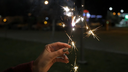 Beautiful sparkler in woman hand on black or street background. Woman holding sparkler against...