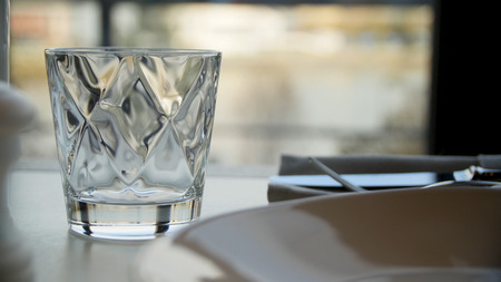 Faceted glass of water on nature background. Clear faceted glass with whiskey on a dark wooden table, close-up. Empty faceted glassの写真素材