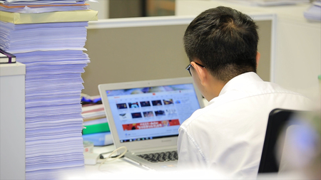 Asian man working on a laptop. Young pensive Asian man working on laptop at office, business or...