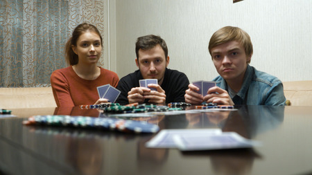 Leisure, games and lifestyle concept - happy friends playing poker at home. Man looks on the cards and makes the betの写真素材