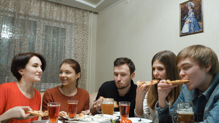 Happy Friends Having Fun At Dinner Party At Home. People Eating Pizza, Drinking Beer And Celebrating...