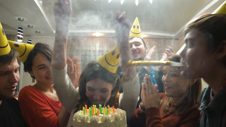 Happy Smiling Girl Blowing Candles out on her Birthday Cake. Girl Surrounded by Her Family and...