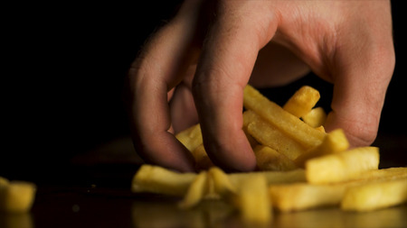 Man's hand eagerly takes fries off the table. Sliced Potatoes on a Cutting Board. Close up view. Delicious French fries, beautifully decorated, is on the table, concept of fast food.の写真素材