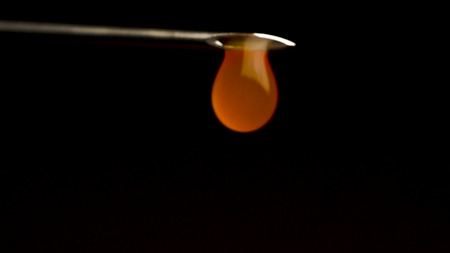 With a needle from a syringe dripping liquid, close-up. Blood flows from syringe on a black background. With a syringe dripping red liquid.の写真素材