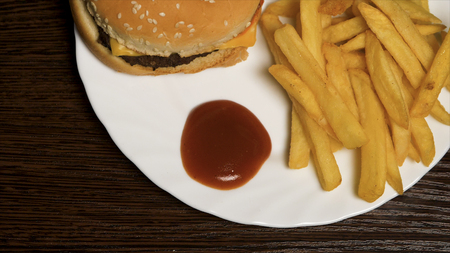French fries with ketchup and hamburger. Cheeseburger with french fries on a white plate. Delicious fast food.の写真素材