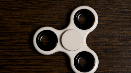 White spinner is spinning on the table. Spinning in motion of a popular white toy spinner on a wooden table. Developing, meditation, relaxation.の写真素材