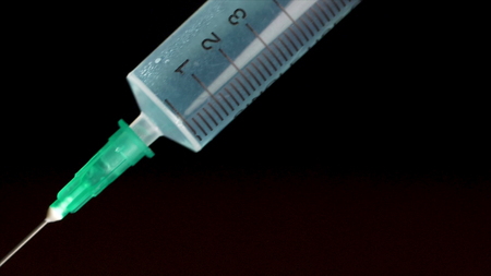 Medical syringe with liquid on black background. Water drop from syringe needle. Close up. research scientist hand with white glove and cylinder blue tintedの写真素材